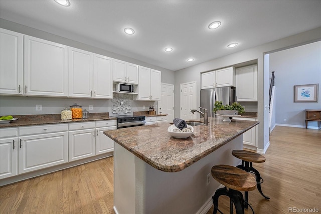 kitchen with light wood-style flooring, a sink, white cabinetry, appliances with stainless steel finishes, and a kitchen bar