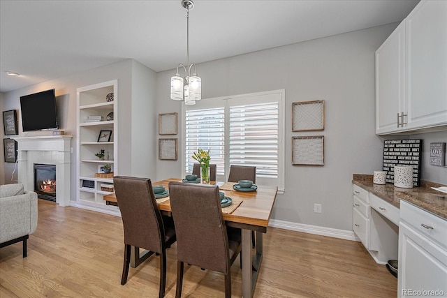 dining space featuring a notable chandelier, built in features, baseboards, light wood finished floors, and a glass covered fireplace