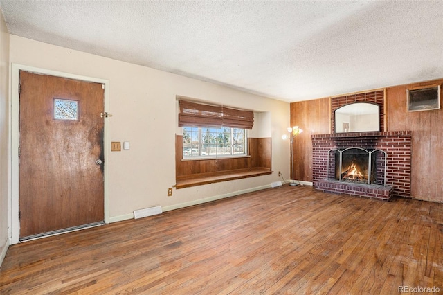 unfurnished living room with a textured ceiling, wood-type flooring, visible vents, and a brick fireplace