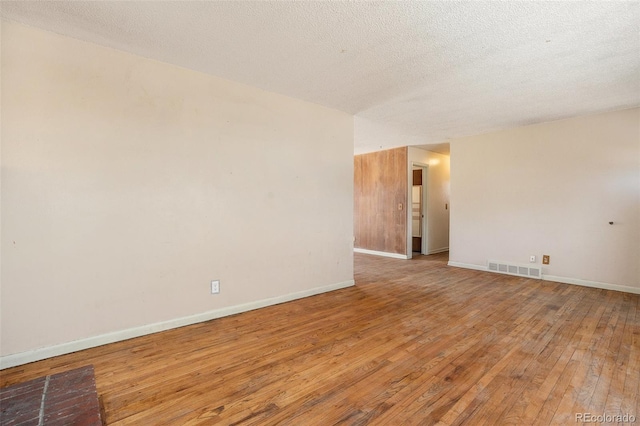 empty room featuring baseboards, a textured ceiling, visible vents, and light wood-style floors