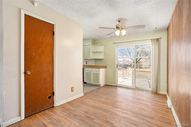 interior space featuring a textured ceiling, baseboards, a ceiling fan, and light wood-style floors