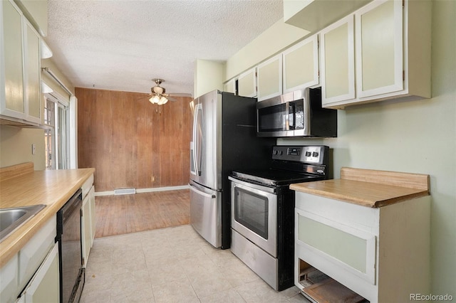 kitchen with a textured ceiling, ceiling fan, stainless steel appliances, wood walls, and light countertops