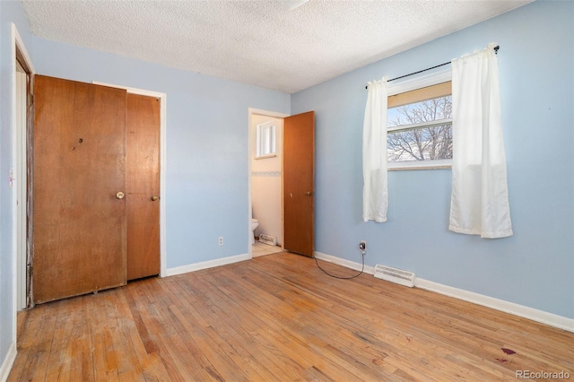 unfurnished bedroom with a textured ceiling, visible vents, baseboards, hardwood / wood-style floors, and ensuite bath