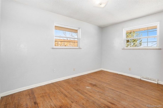 empty room with a textured ceiling, hardwood / wood-style flooring, visible vents, and baseboards