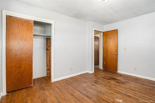 unfurnished bedroom featuring a textured ceiling, hardwood / wood-style floors, a closet, and baseboards