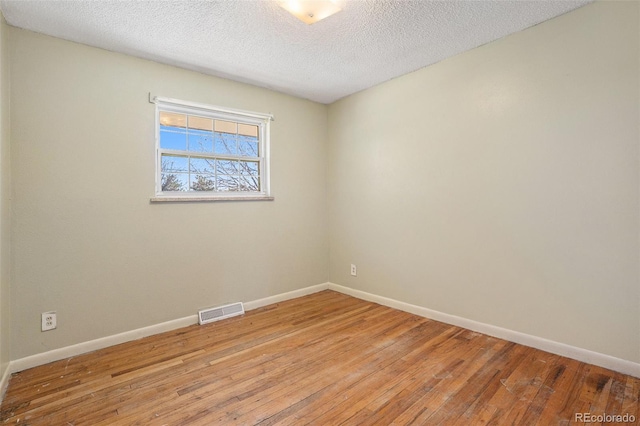 unfurnished room with a textured ceiling, light wood finished floors, visible vents, and baseboards