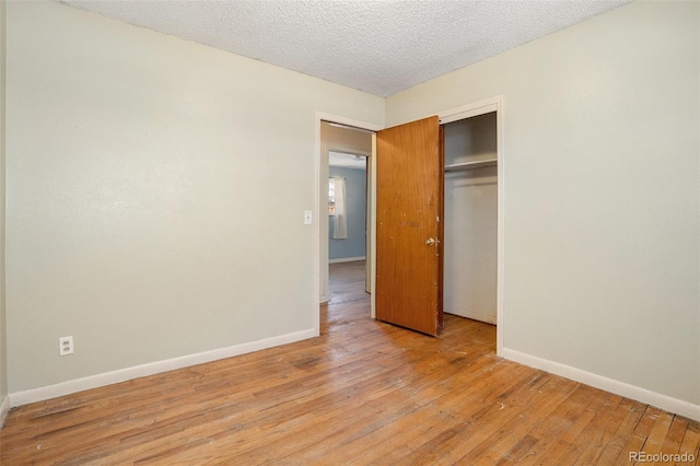 unfurnished bedroom with light wood-type flooring, a closet, baseboards, and a textured ceiling