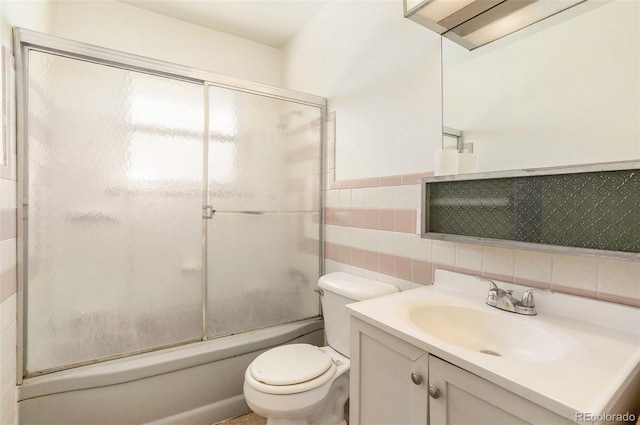 full bathroom with tile walls, toilet, enclosed tub / shower combo, vanity, and a wealth of natural light