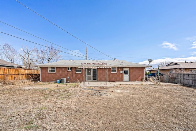 rear view of house with a fenced backyard, brick siding, central AC unit, and a patio