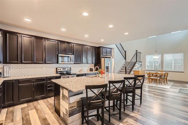 6883 E 132nd Pl, Thornton, CO 80602 - kitchen featuring stainless steel appliances, light stone countertops, a breakfast bar, light wood-style floors, and recessed lighting