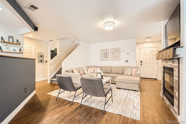 living room with stairs, visible vents, a tiled fireplace, and wood finished floors