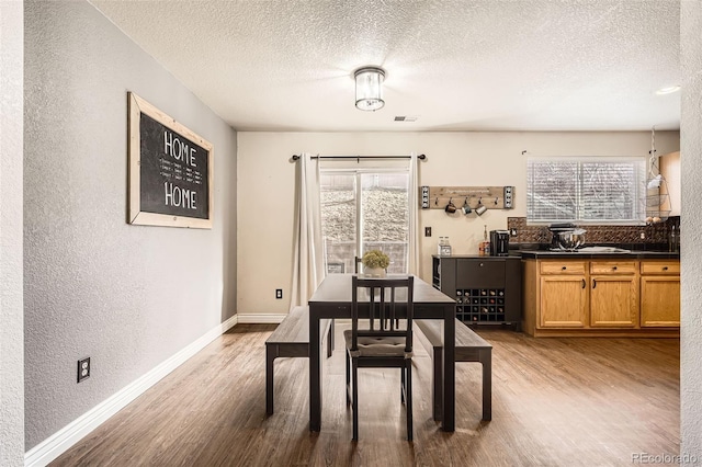 dining area featuring a textured wall, plenty of natural light, wood finished floors, and baseboards