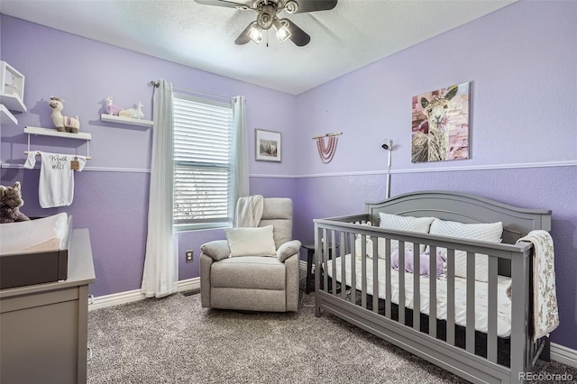 carpeted bedroom featuring a textured ceiling, ceiling fan, a textured wall, baseboards, and a crib