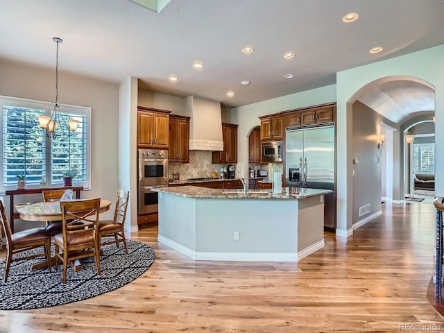 5092 S Allison Way, Littleton, CO 80123 - kitchen with built in appliances, arched walkways, light wood-style floors, light stone countertops, and a center island with sink
