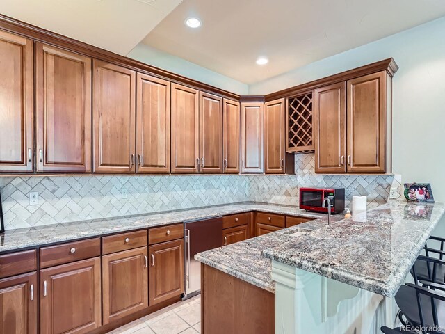 5092 S Allison Way, Littleton, CO 80123 - kitchen with a breakfast bar area, a peninsula, light stone countertops, decorative backsplash, and brown cabinets