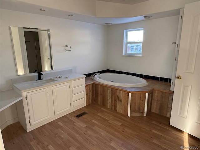 bathroom featuring hardwood / wood-style flooring, vanity, and tiled tub