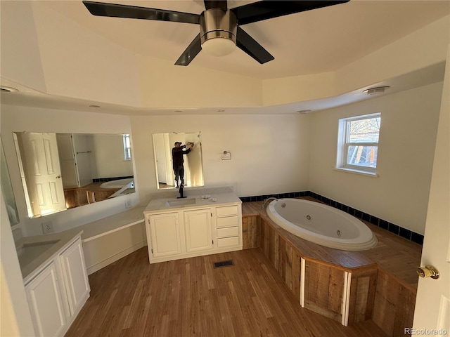 bathroom with tiled tub, wood-type flooring, vanity, and ceiling fan