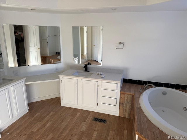 bathroom with vanity, a relaxing tiled tub, and wood-type flooring