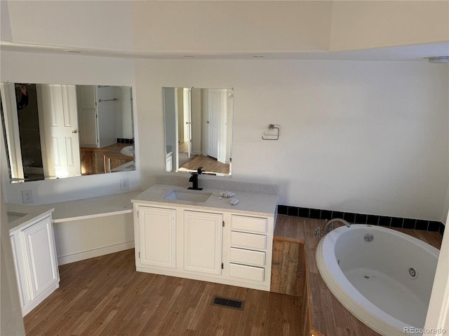 bathroom featuring hardwood / wood-style flooring, vanity, and tiled tub