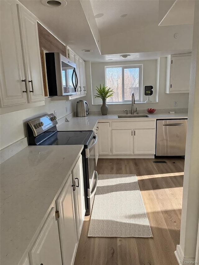 kitchen with stainless steel appliances, sink, hardwood / wood-style floors, and white cabinets