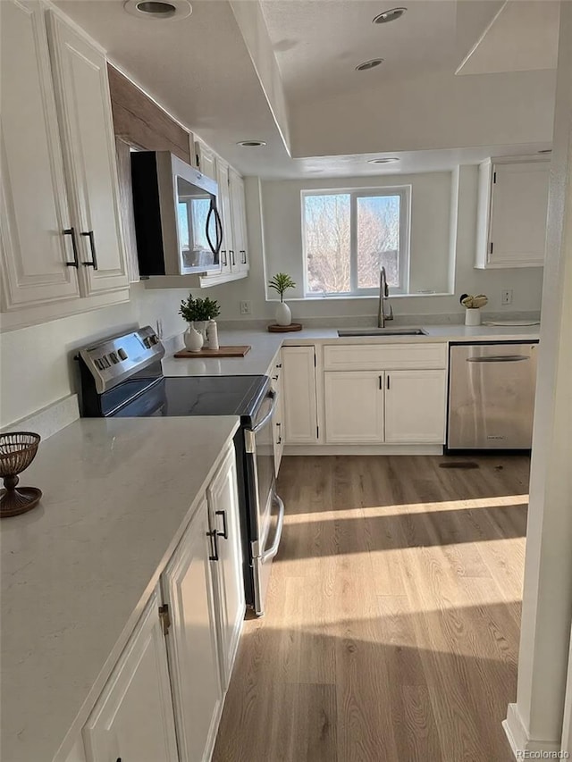 kitchen with white cabinetry, appliances with stainless steel finishes, sink, and light wood-type flooring