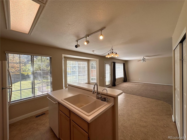 kitchen with a textured ceiling, a kitchen island with sink, stainless steel dishwasher, sink, and white refrigerator