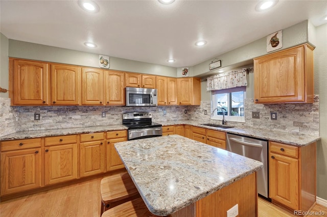 kitchen featuring appliances with stainless steel finishes, a sink, light stone countertops, light wood finished floors, and a kitchen island