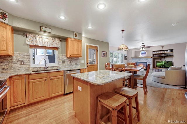 kitchen featuring stainless steel appliances, a sink, a fireplace, light wood finished floors, and backsplash