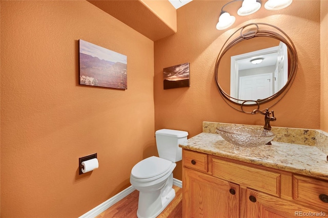 half bath featuring wood finished floors, toilet, vanity, and baseboards