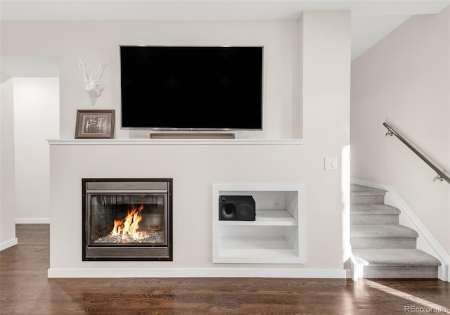 room details featuring baseboards, a glass covered fireplace, wood finished floors, and built in features