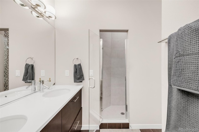 bathroom featuring baseboards, double vanity, a sink, and a shower stall