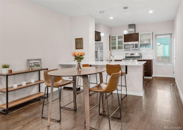 kitchen with dark wood-style flooring, stainless steel appliances, light countertops, glass insert cabinets, and a peninsula