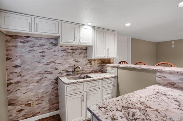 8951 Greenwich St, Highlands Ranch, CO 80130 - kitchen with a sink, recessed lighting, light stone counters, decorative backsplash, and white cabinetry