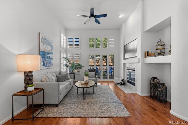 9491 Southern Hills Cir, Lone Tree, CO 80124 - living area featuring a tiled fireplace, wood finished floors, ceiling fan, and a towering ceiling