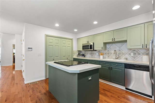 9491 Southern Hills Cir, Lone Tree, CO 80124 - kitchen featuring green cabinetry, appliances with stainless steel finishes, a center island, wood finished floors, and decorative backsplash