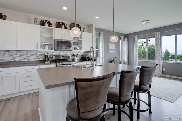10906 Touchstone Loop, Parker, CO 80134 - kitchen with stainless steel appliances, open shelves, light wood-style floors, a center island with sink, and recessed lighting