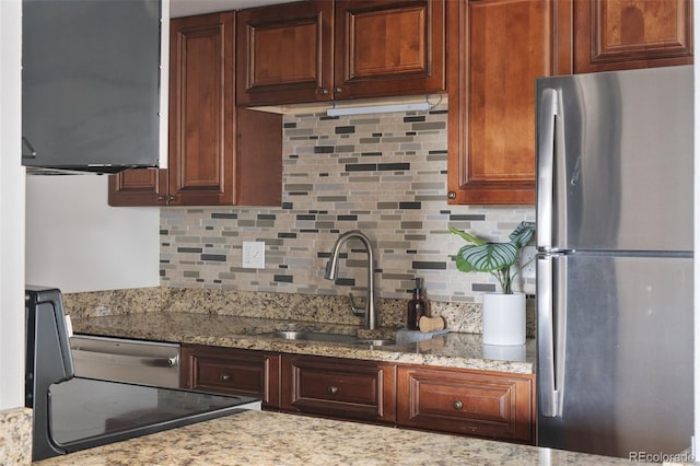 kitchen featuring sink, light stone counters, stainless steel fridge, decorative backsplash, and stove