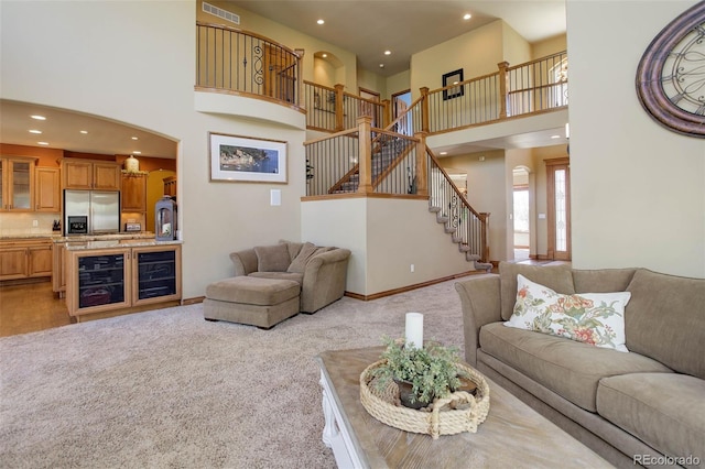 carpeted living area featuring stairs, a high ceiling, visible vents, and recessed lighting