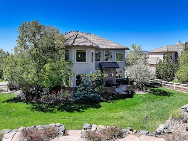 back of property featuring a tiled roof, stucco siding, fence, and a lawn