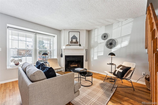 living area featuring a textured ceiling, a fireplace, baseboards, and wood finished floors