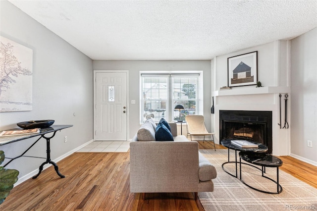 living area featuring light wood finished floors, a fireplace with flush hearth, baseboards, and a textured ceiling