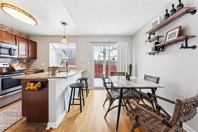 kitchen featuring light stone counters, light wood-style flooring, appliances with stainless steel finishes, tasteful backsplash, and pendant lighting