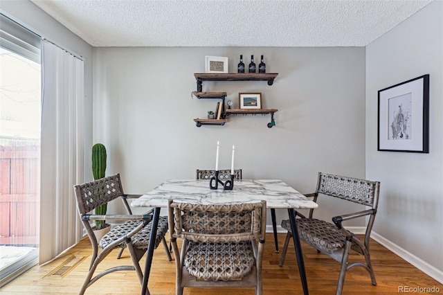 dining area featuring visible vents, a textured ceiling, baseboards, and wood finished floors