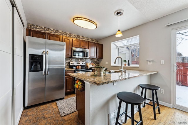 kitchen featuring light stone counters, a peninsula, hanging light fixtures, stainless steel appliances, and a sink