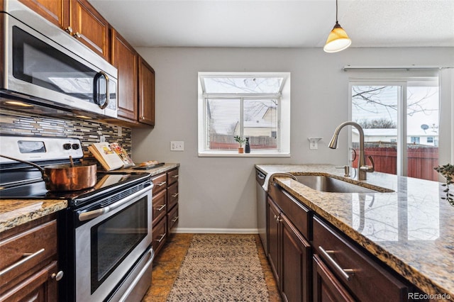 kitchen with a wealth of natural light, appliances with stainless steel finishes, light stone counters, and pendant lighting