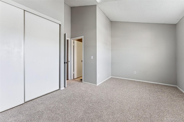 unfurnished bedroom with a closet, light colored carpet, a textured ceiling, and baseboards