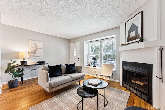 living area with a glass covered fireplace, baseboards, a textured ceiling, and light wood finished floors