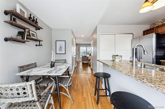 kitchen with stainless steel fridge, light stone counters, light wood-type flooring, a kitchen bar, and open shelves