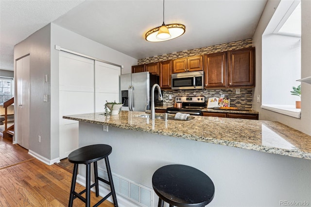 kitchen featuring a peninsula, appliances with stainless steel finishes, light stone countertops, and pendant lighting