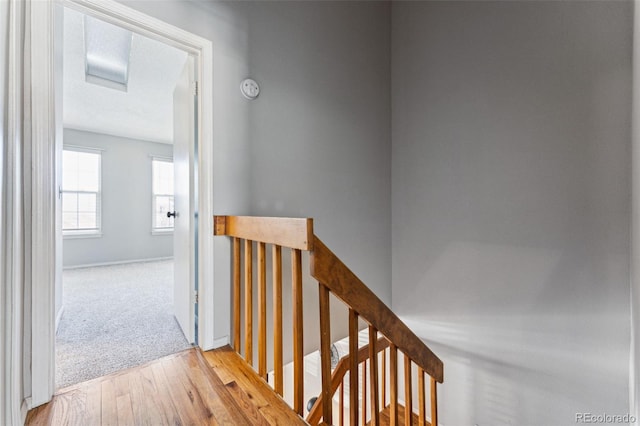 hall featuring light wood-type flooring, an upstairs landing, and baseboards